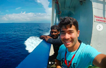 A smiling handsome young man with blue water and boat.