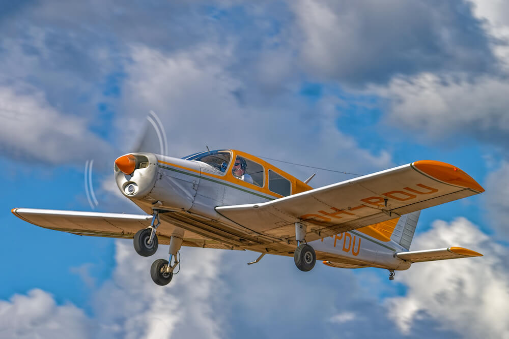 A
beautiful small Piper aircraft painted orange and white, flying in a blue sky
with clouds.
